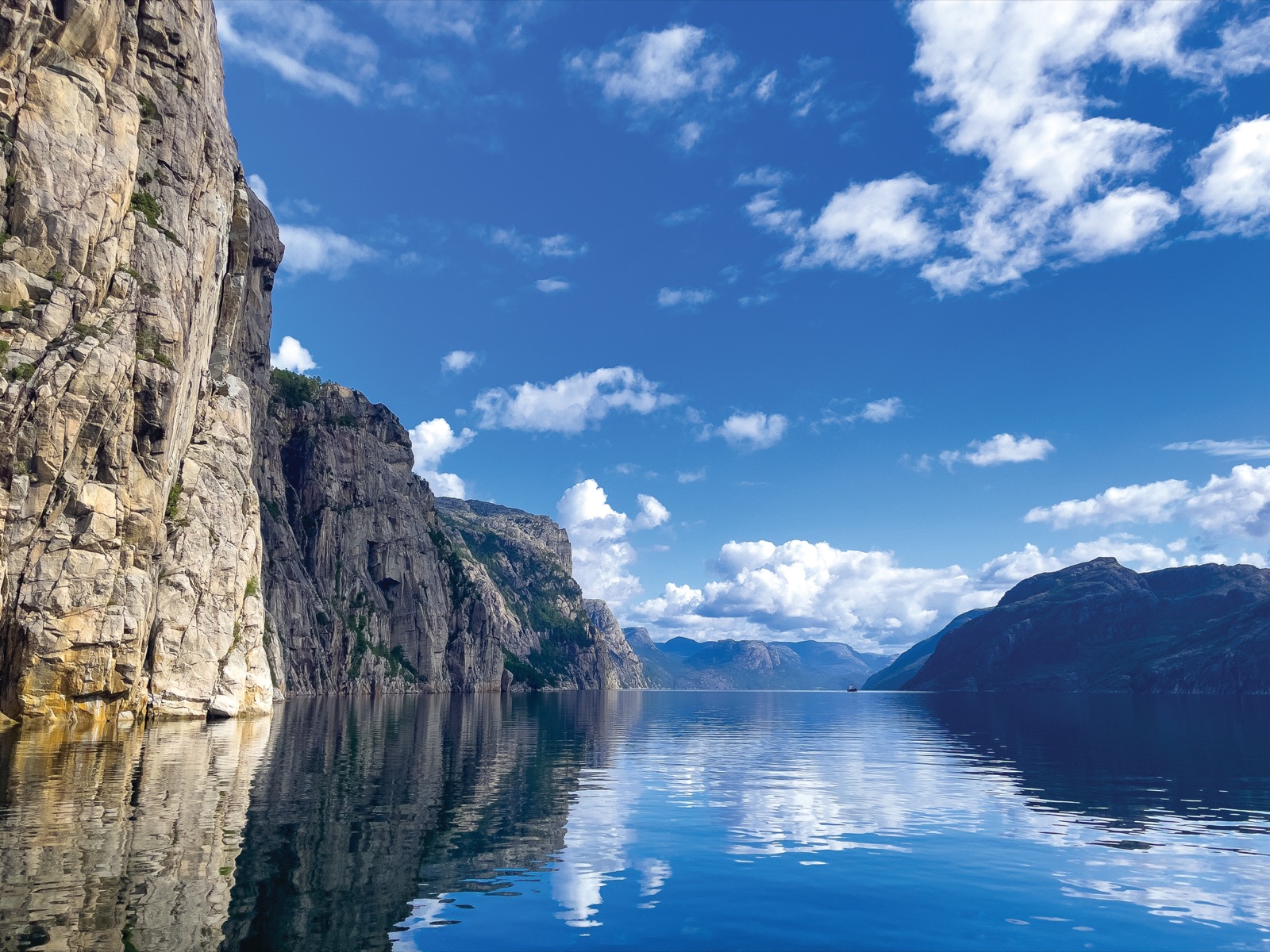 Sheer cliffs rising from the calm Lysefjord under a blue sky